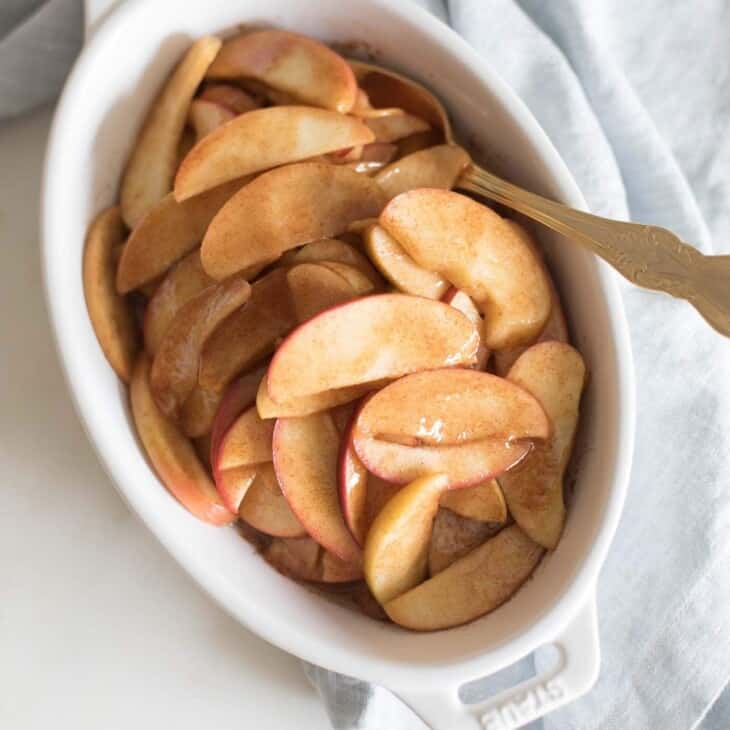 一个白色的椭圆形烤盘里盛满了烤苹果片，金色的勺子从边上伸出来。gydF4y2Ba
