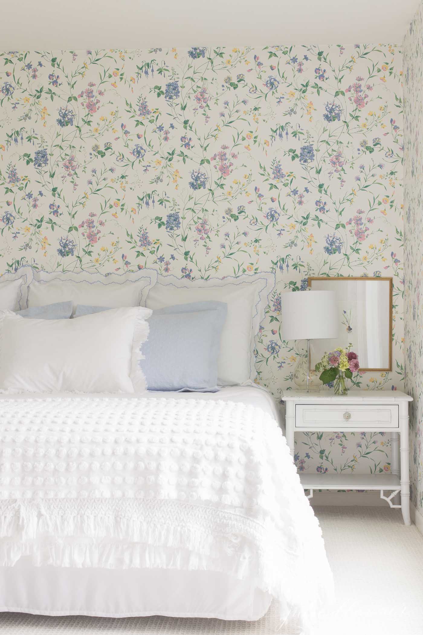 一间花墙纸的客人卧室，带有蓝色和白色的床上用品。