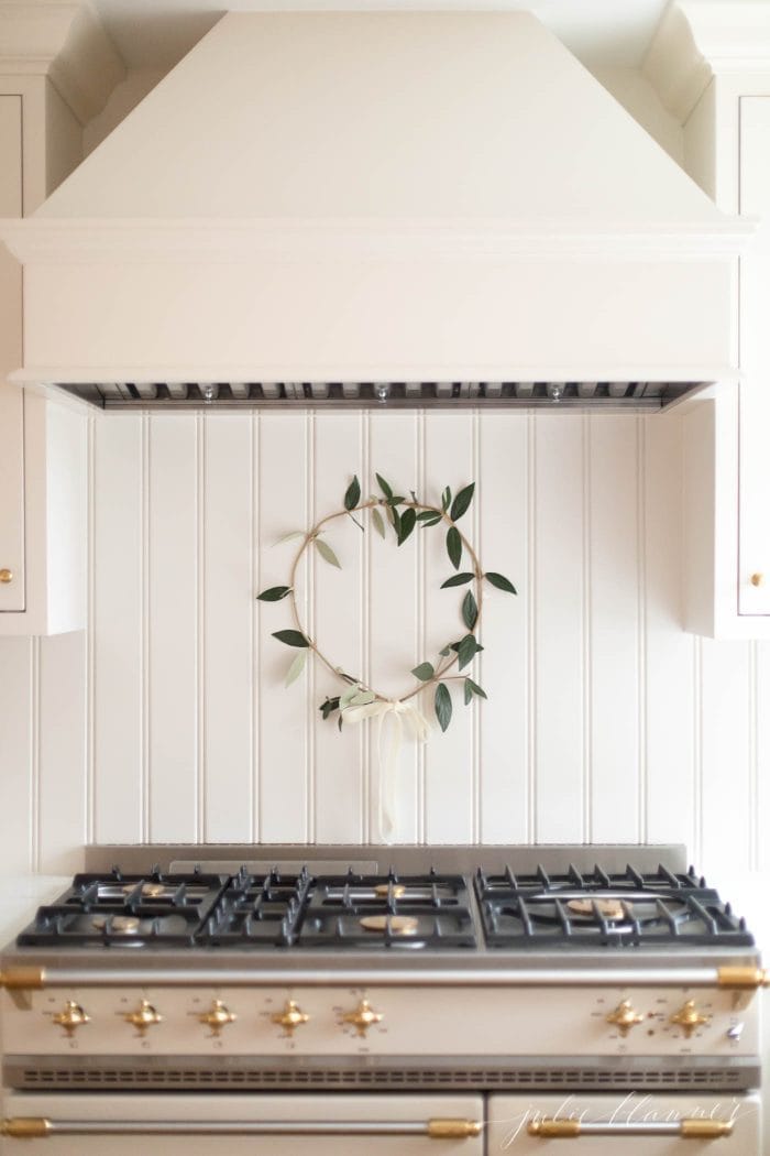 一间奶油色的厨房，灶台后面挂着一个简单的绿色花环。