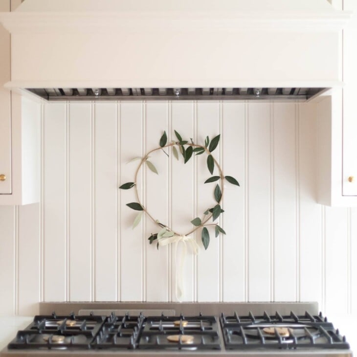 奶油色厨房，炉灶后面挂着一个简单的绿色花环。