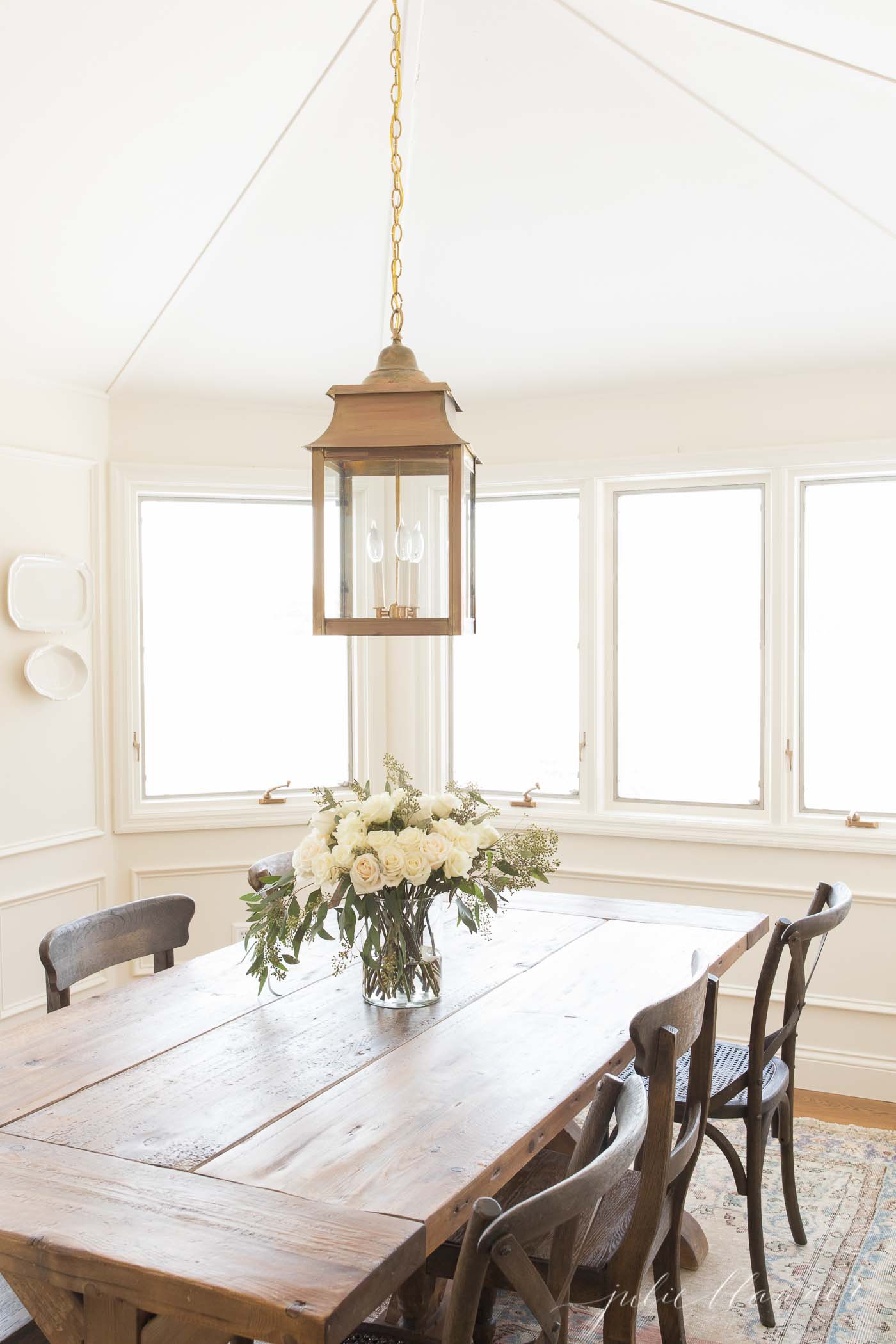 有农场桌和黄铜枝形吊灯的白色餐厅，在桌上的白花。