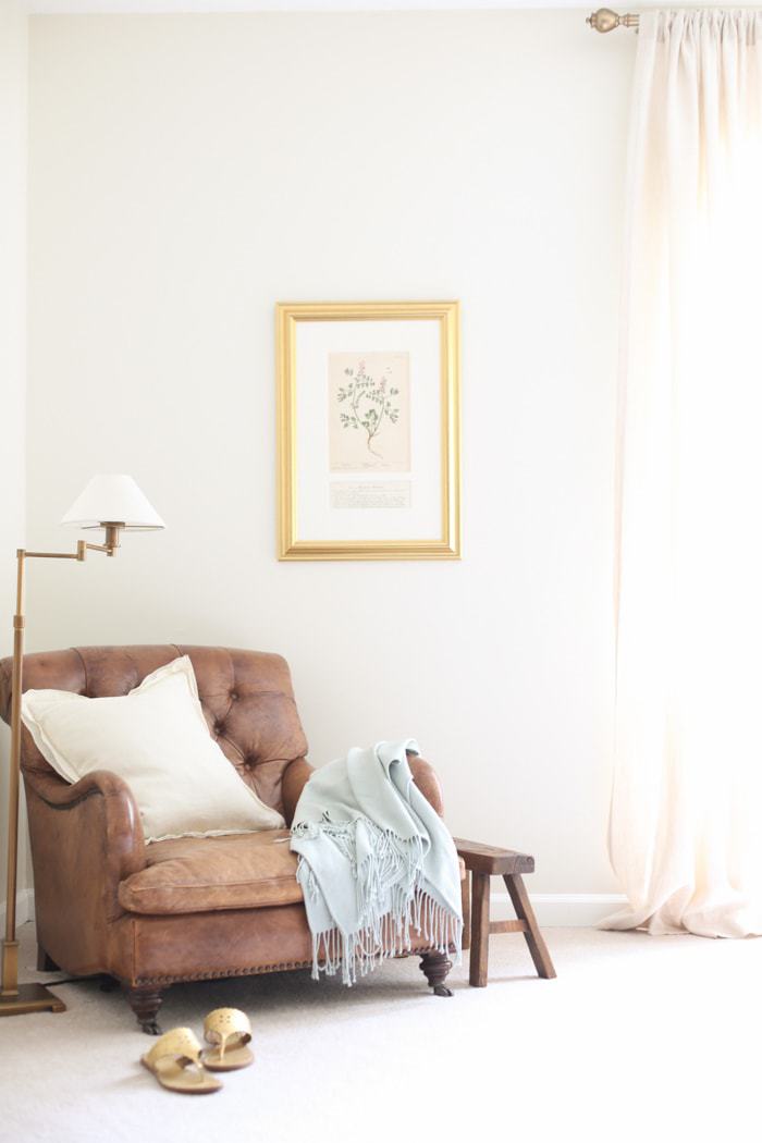 卧室角落里有一把皮革古董椅子，墙壁上刷着奶油色油漆，装饰漆是白色的。