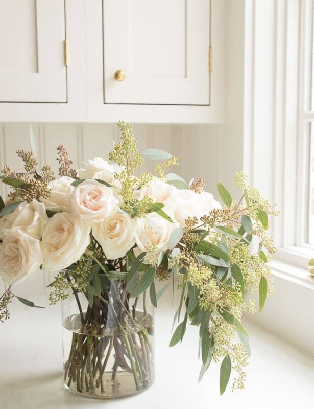 奶油厨房背景和简单的透明圆柱花瓶，里面装满了玫瑰和桉树。