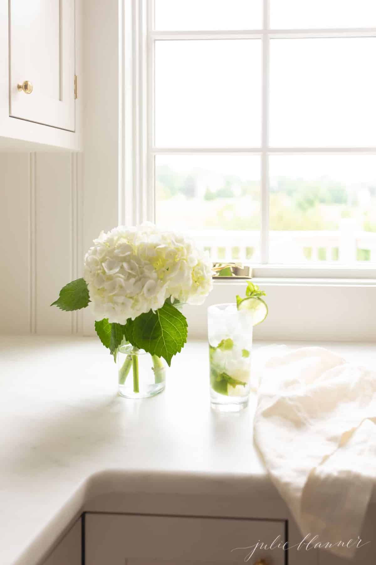 白色台面配有绣球花瓶和带有莫吉托的高大透明玻璃。GydF4y2Ba
