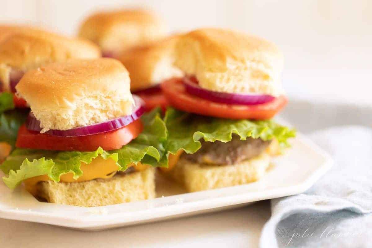 夹着生菜、西红柿和洋葱的汉堡放在一个白色的浅盘上。# burgersintheoven