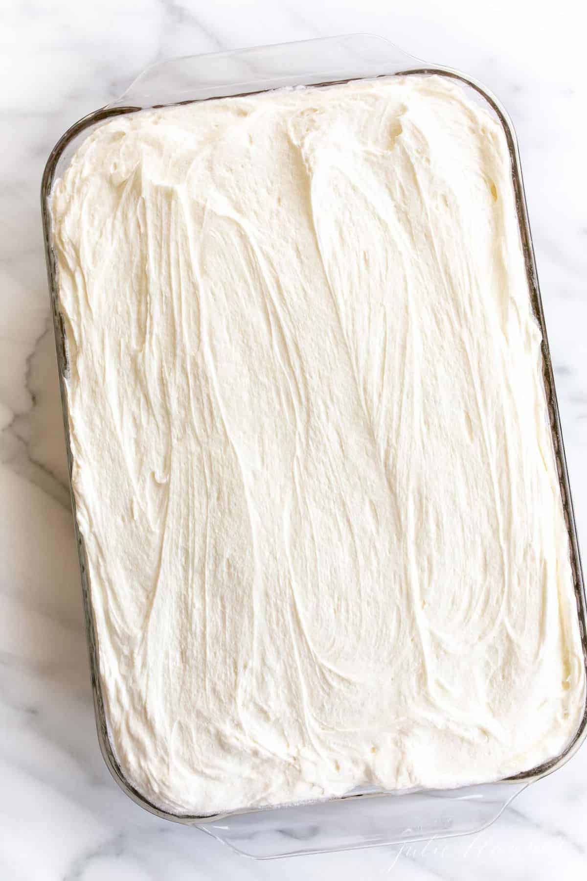 在大理石表面的玻璃烤盘里，覆盖着白色糖霜的蓬松蛋糕。
