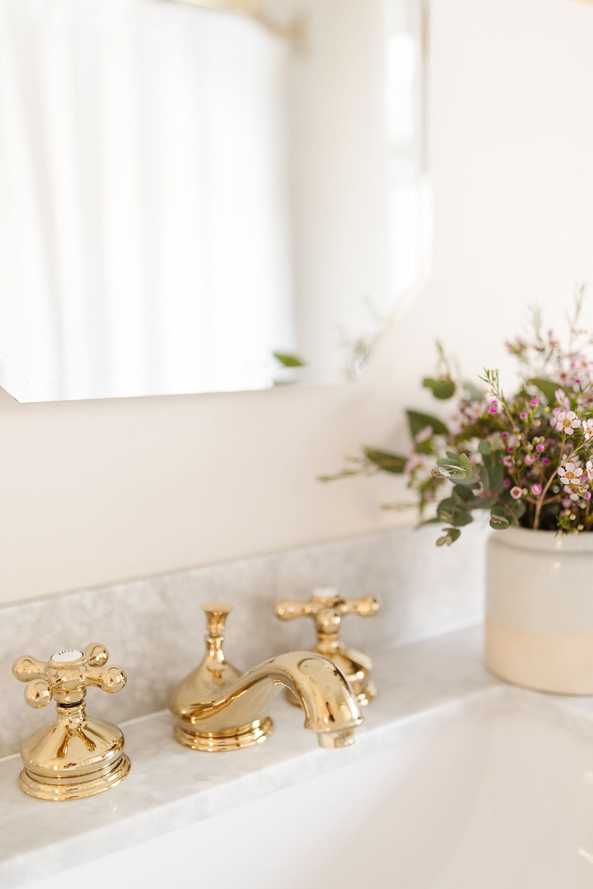 一个金色的水龙头放在大理石的梳妆台上，背景是鲜花
