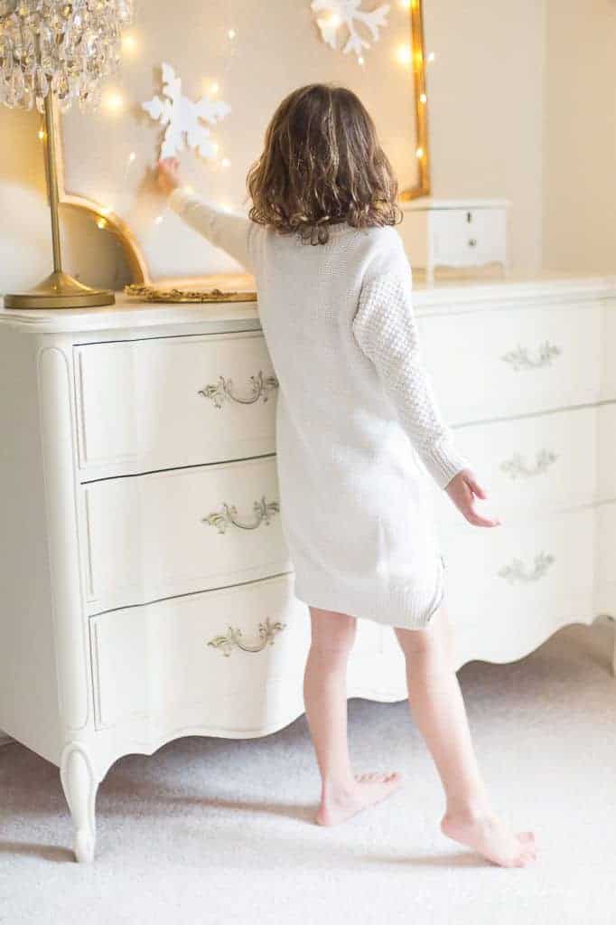 一个小女孩穿着白色的衣服，在她白色的卧室里挂着纸雪花作为简单的圣诞节装饰。