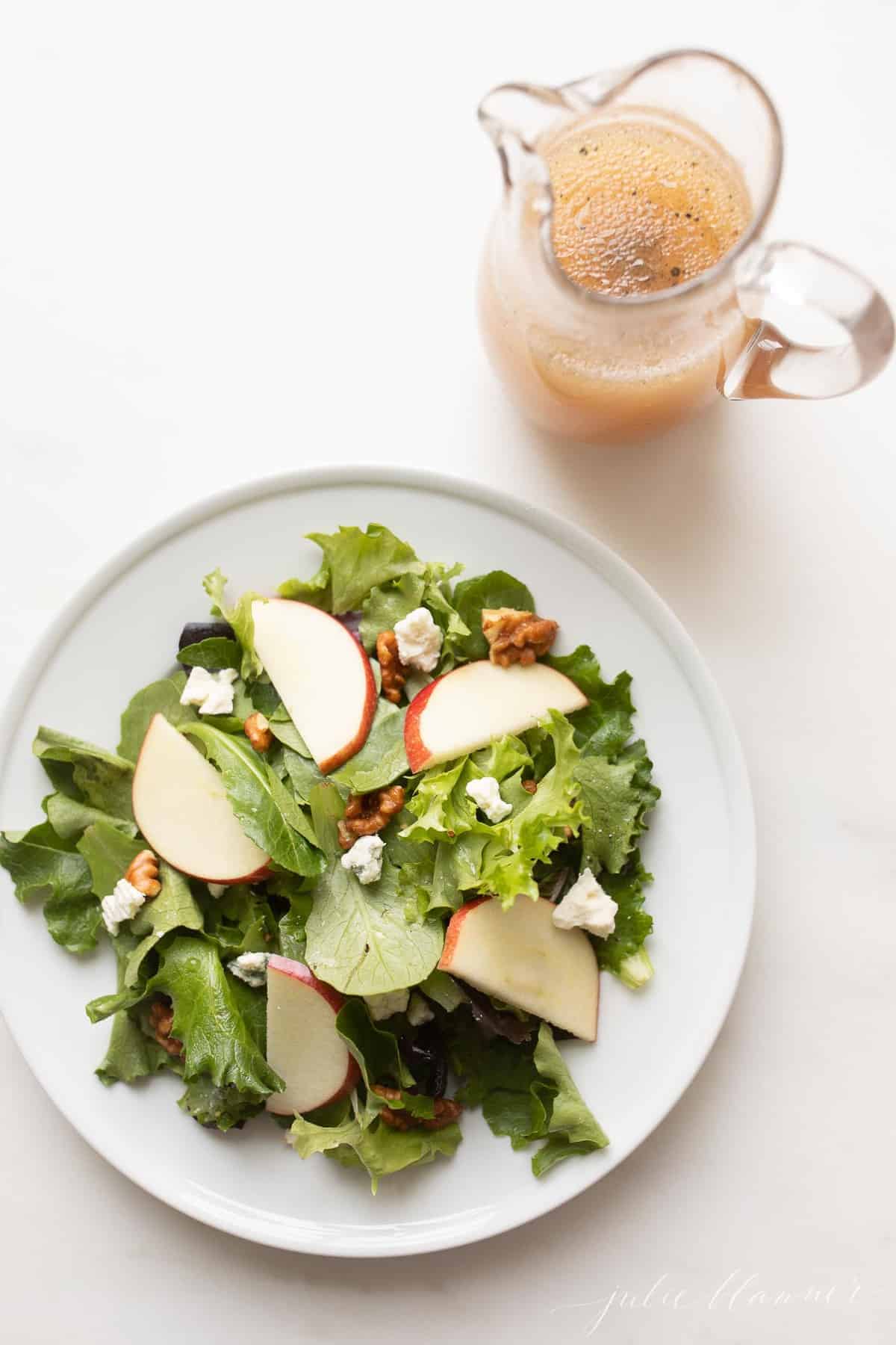 白色的表面，白色的盘子上有绿叶沙拉和苹果片。