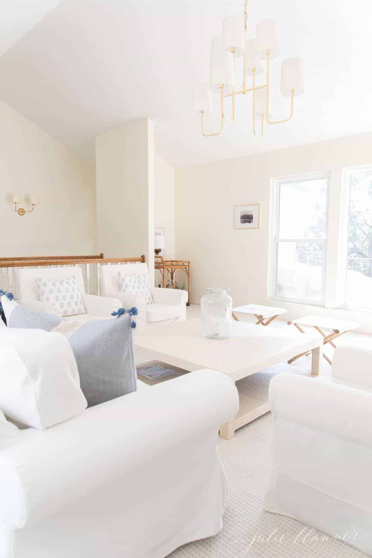 白色客厅，带有白色沙发和大米色咖啡桌，上面的黄铜吊灯。