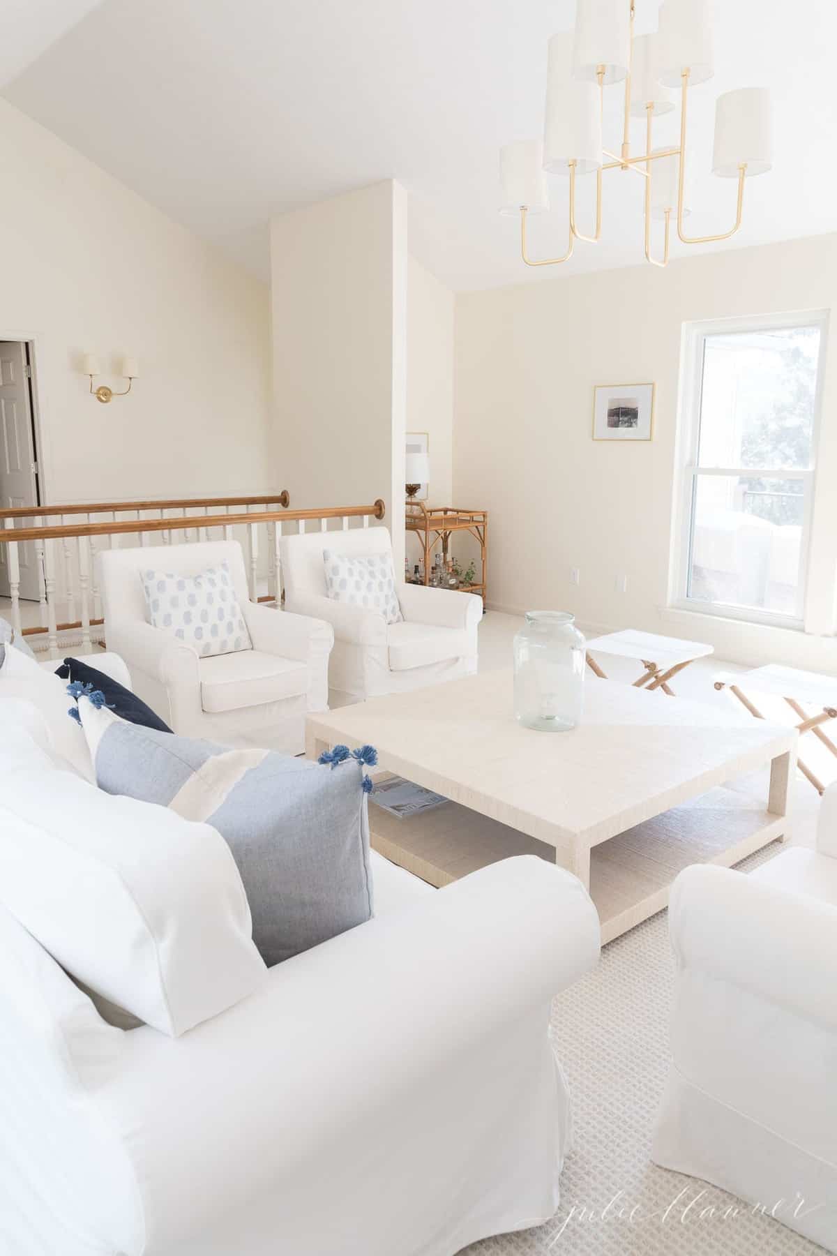 白色客厅，带有白色宜家Ektorp沙发和大型米色咖啡桌，上面的黄铜吊灯。