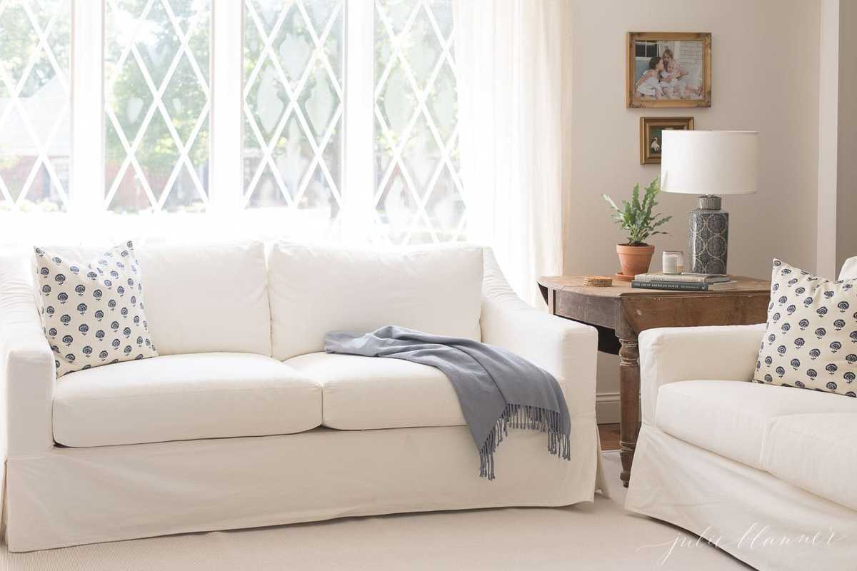 白色的陶瓷谷仓沙发，蓝色的毯子，古色古香的木桌，蓝色的灯和简单的装饰在客厅。