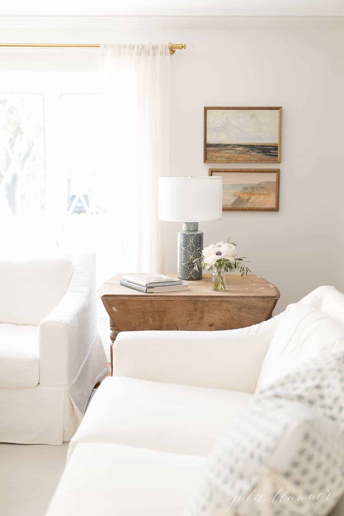 白色陶器谷仓(White Pottery Barn)的沙发，古董木桌和一盏蓝色台灯，客厅里装饰简单。