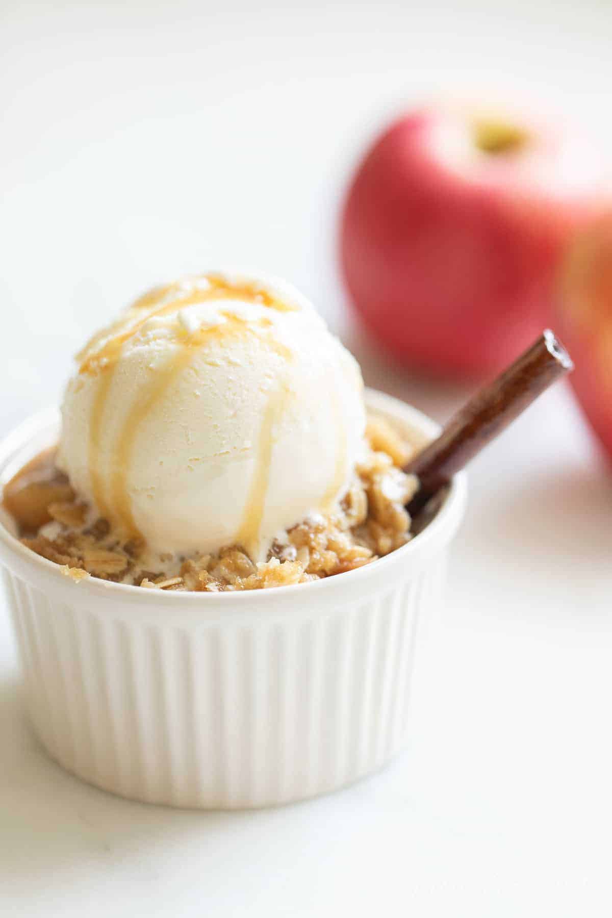 白色的表面上有一小块白色的苹果脆片，上面有一勺香草冰淇淋和焦糖。背景是苹果。