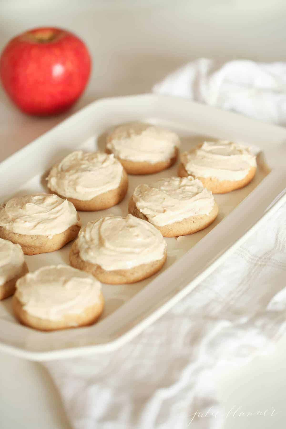 白色托盘放在白色亚麻毛巾上，背景是苹果——托盘上有磨砂苹果糖饼干。