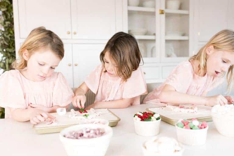 三个小女孩穿着粉红色的衣服，装饰一块饼干，为圣诞节的烘焙礼物做准备