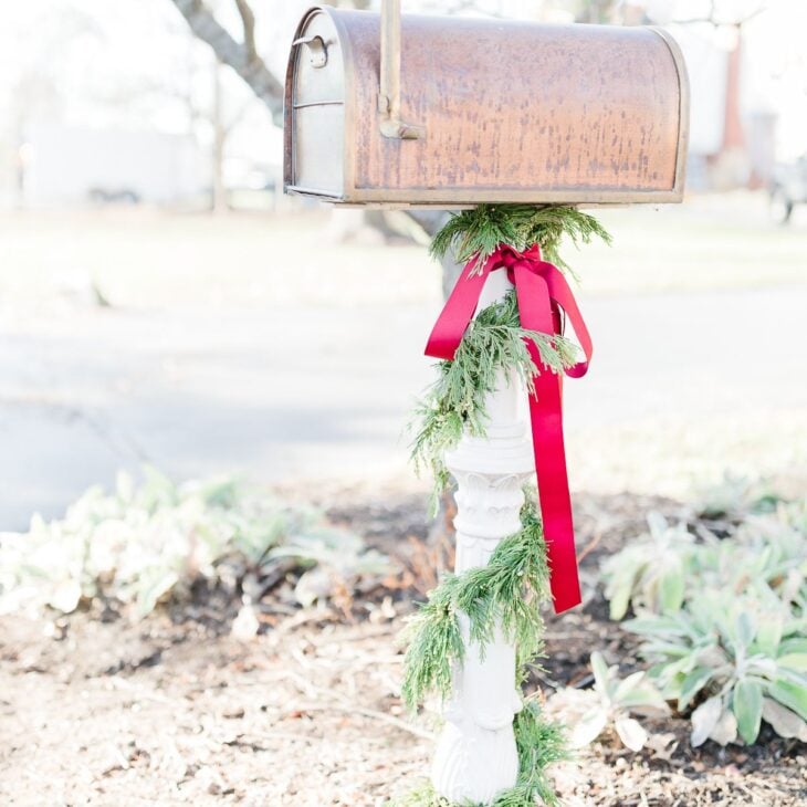 带有雪松花环和红色蝴蝶结的圣诞邮箱装饰的铜邮箱。