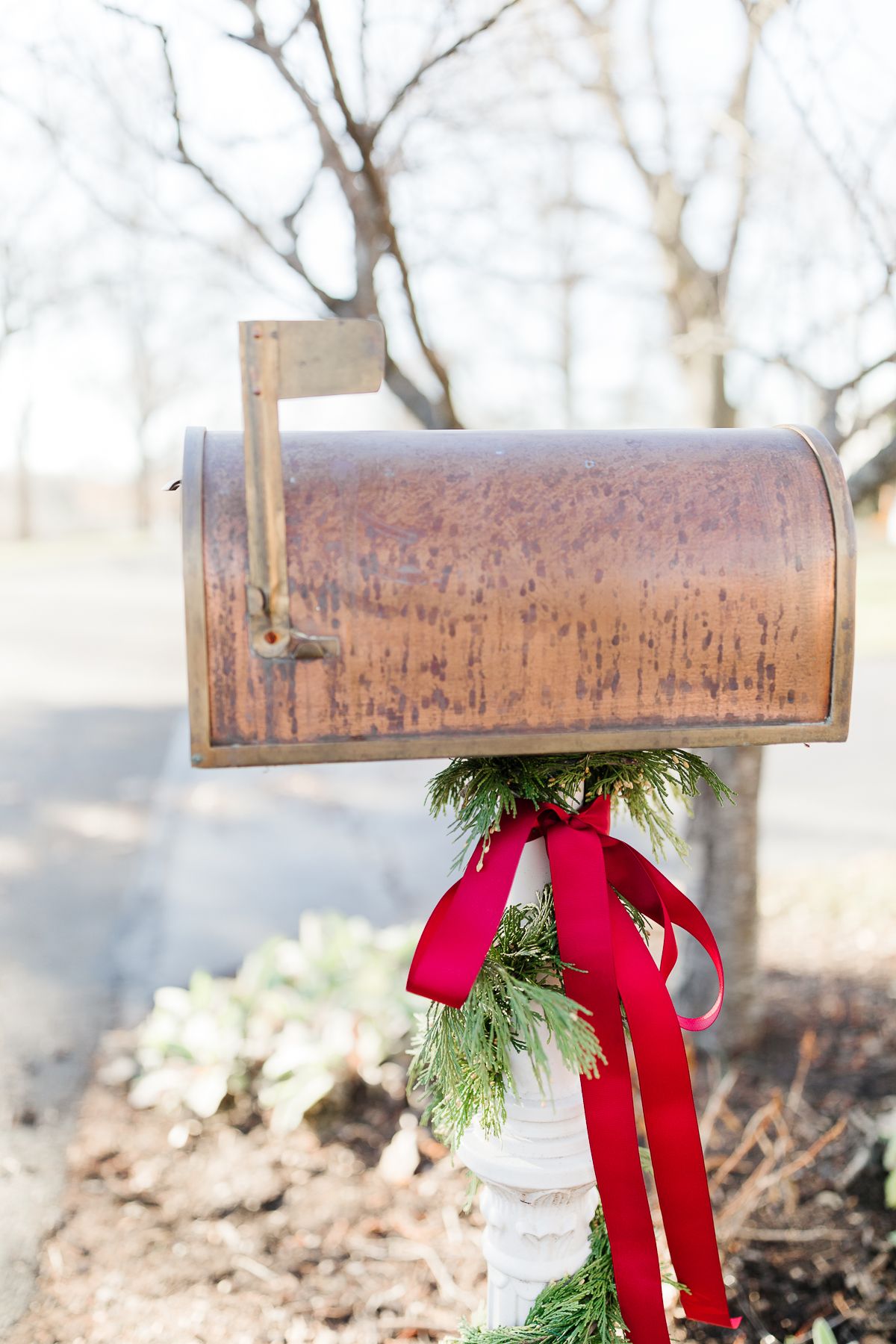 一个铜邮筒，用雪松花环和红色蝴蝶结装饰圣诞邮筒。