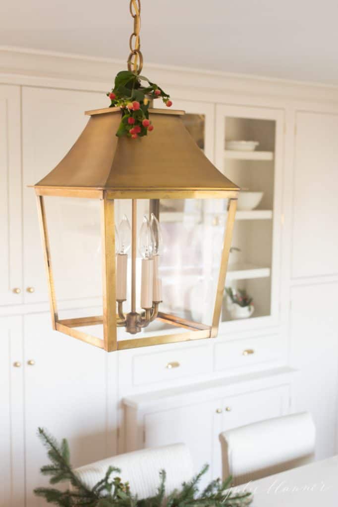 白色厨房里的一盏黄铜灯笼，装饰着一丝绿色的圣诞装饰。