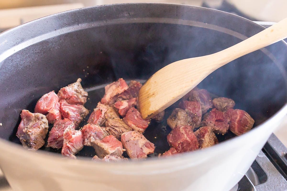 炉子上有一个白色的铸铁锅，用木勺搅拌成褐色的牛肉块。gydF4y2Ba