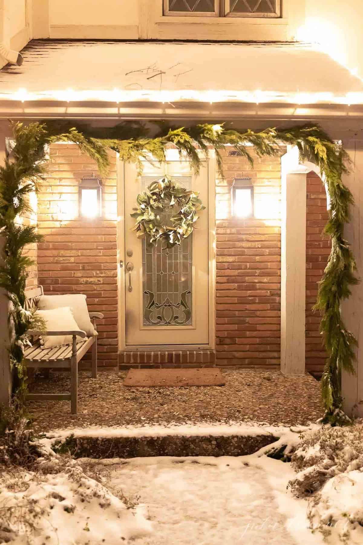 一个家的外观，地面上的雪和绿色的花环在柱子上为圣诞节。