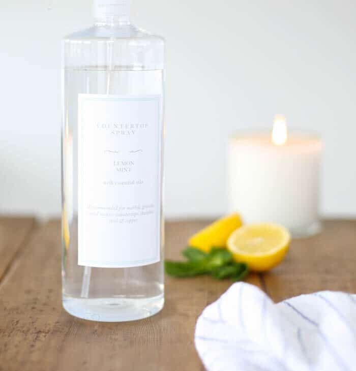 一个透明的玻璃喷雾瓶与定制的标签，充满天然的所有用途的有机清洁剂-柠檬和蜡烛在背景。