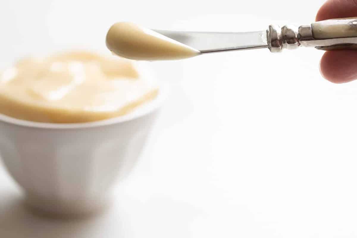 白色的表面，白色的碗里装满了蜂蜜黄油，刀从碗里出来。gydF4y2Ba