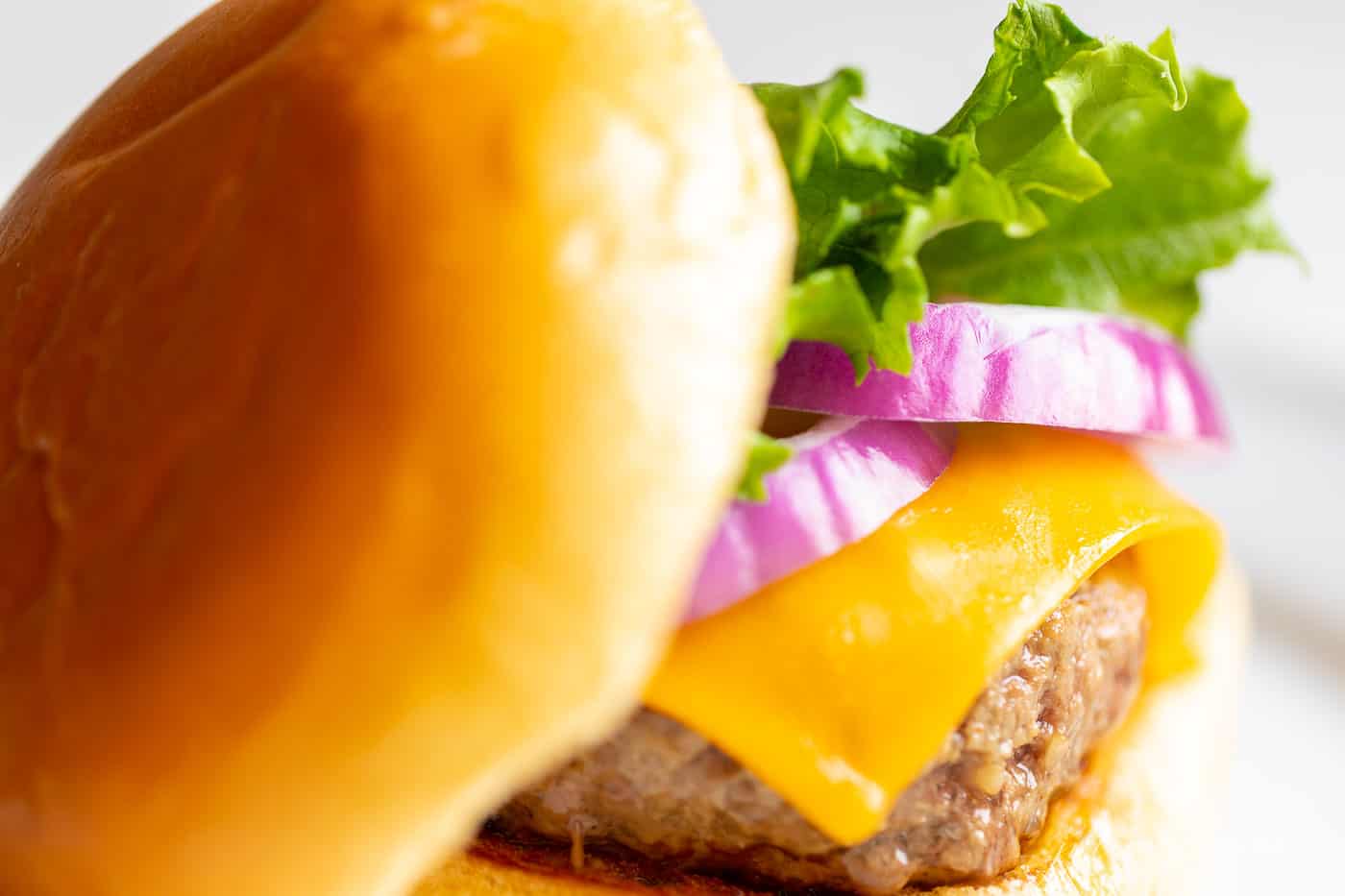 有生菜，乳酪和葱的水多的汉堡在一块白色板材。GydF4y2Ba