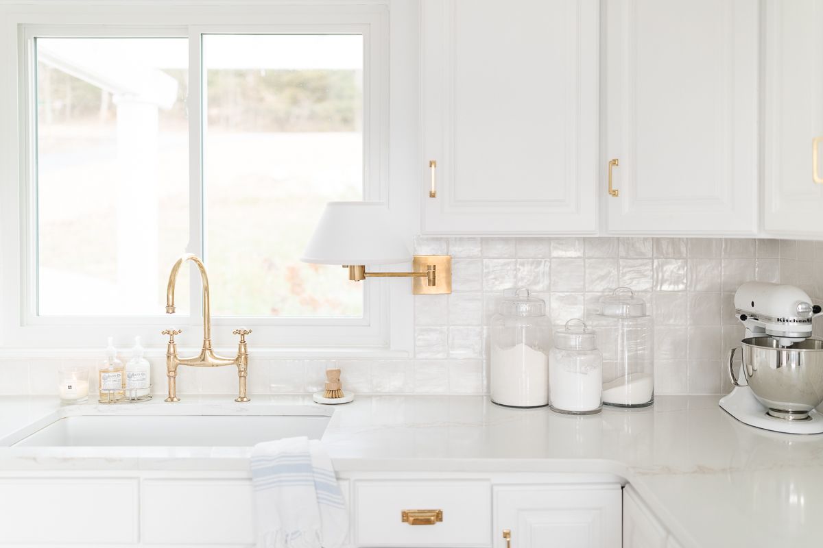 一个白色的厨房，配有玻璃面粉和糖罐和一个白色的厨房辅助搅拌机，用于厨房柜台的组织