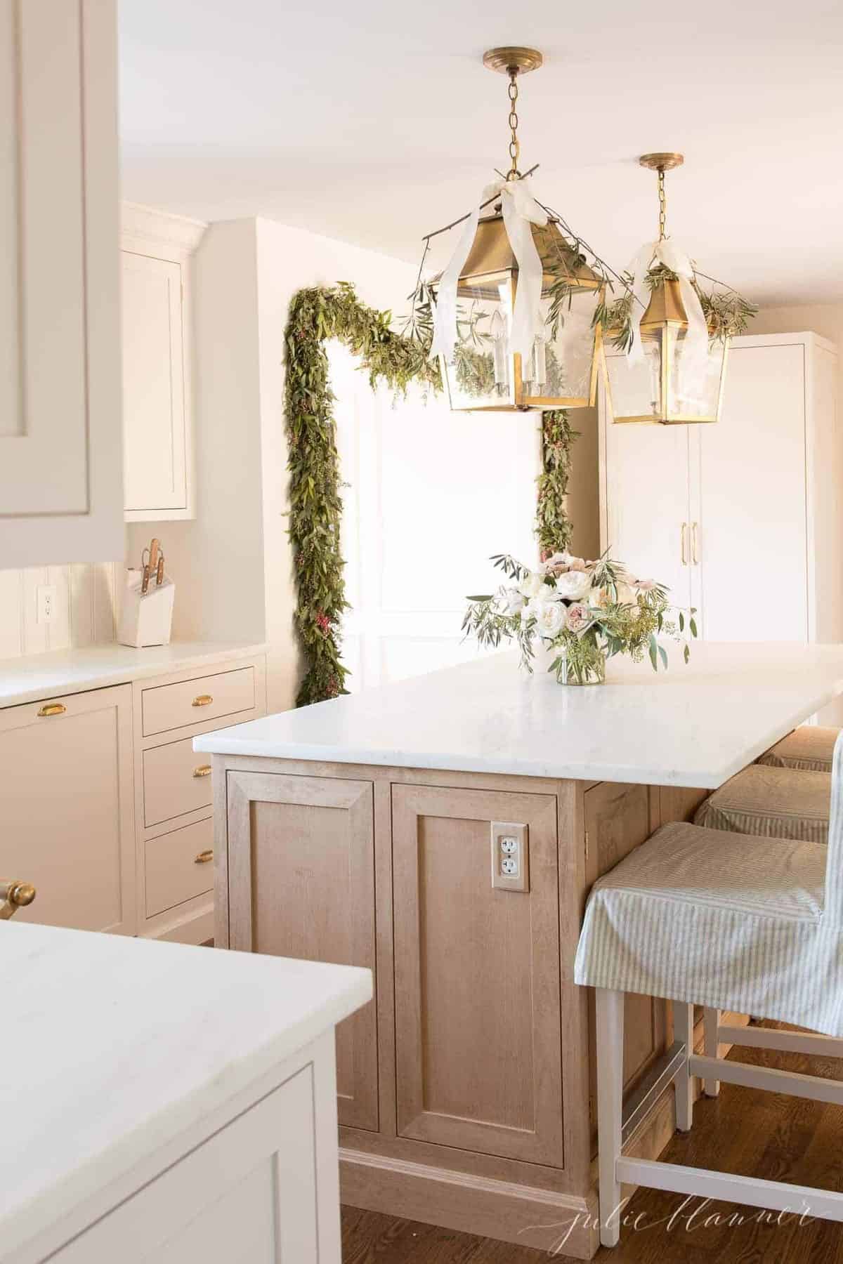 奶油色的厨房里有一个明亮的木岛台，黄铜灯笼，为迎接圣诞节而装饰。