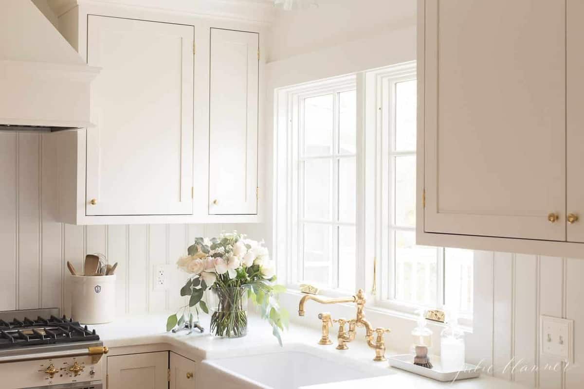 简单的厨房，白色的橱柜，水槽旁放着一瓶花。