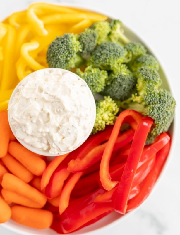 一个充满蔬菜蘸酱的白色碗，周围是切碎的蔬菜。