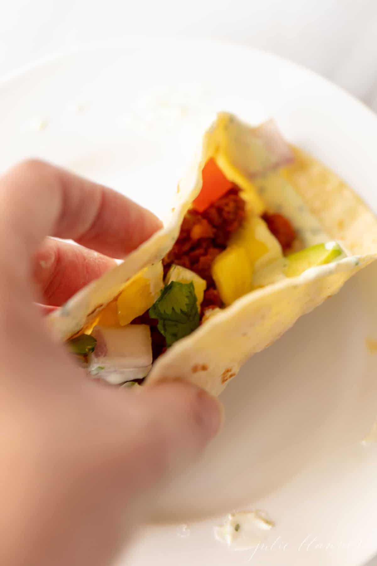 一只手拿着一个墨西哥香肠卷，夹在柔软的玉米饼里。gydF4y2Ba