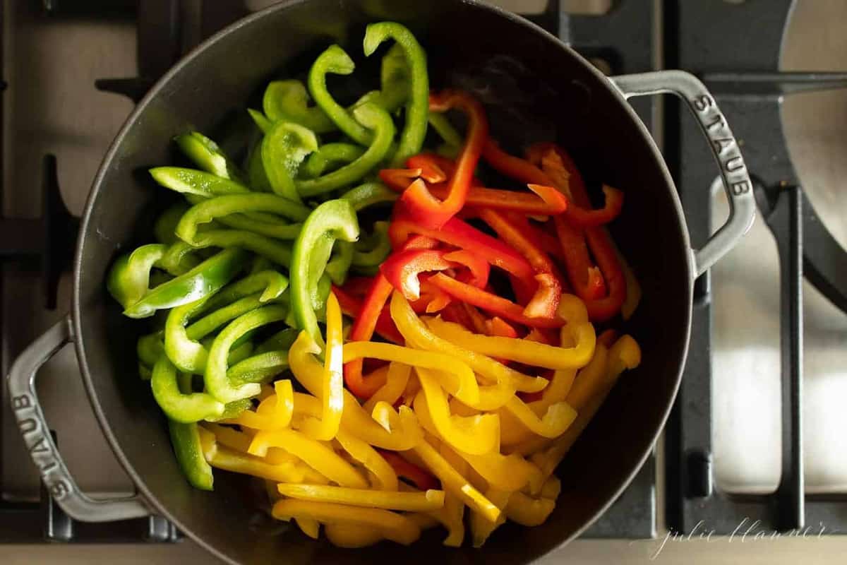 红色，绿色和黄色的甜椒切在炉灶上的锅中。GydF4y2Ba