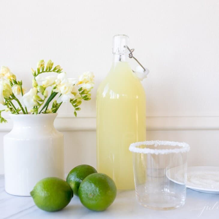 白色厨房背景，充满自制玛格丽塔酒的玻璃玻璃水瓶，酸橙侧面。