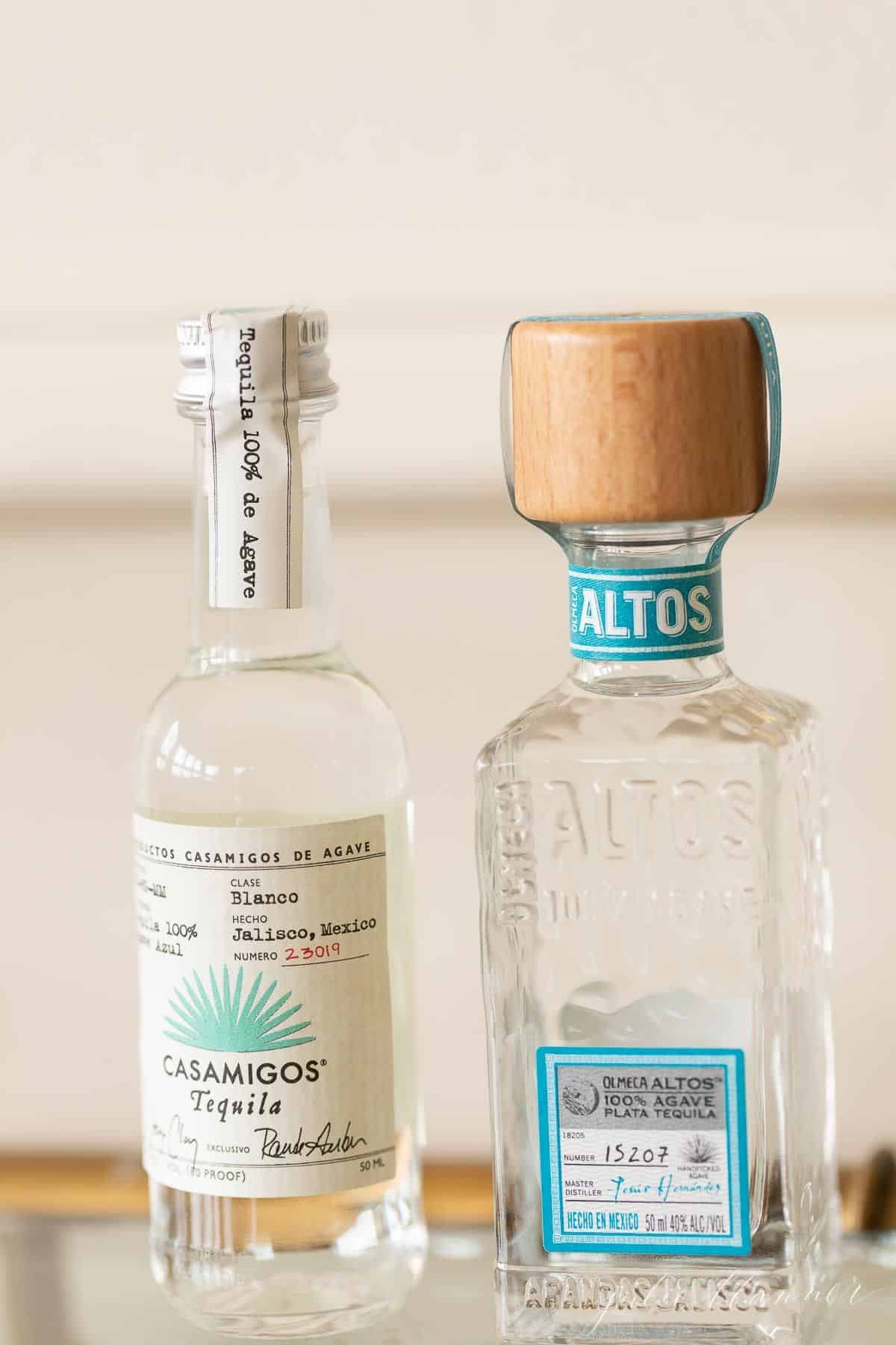 两瓶用来装玛格丽塔酒的透明玻璃龙舌兰酒，放在玻璃酒吧推车上。
