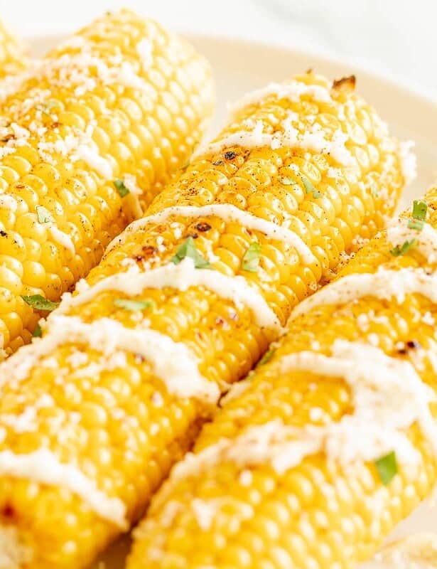 一个白色盘子，上面有三个墨西哥玉米的精美食谱，撒上奶油酱和香菜。