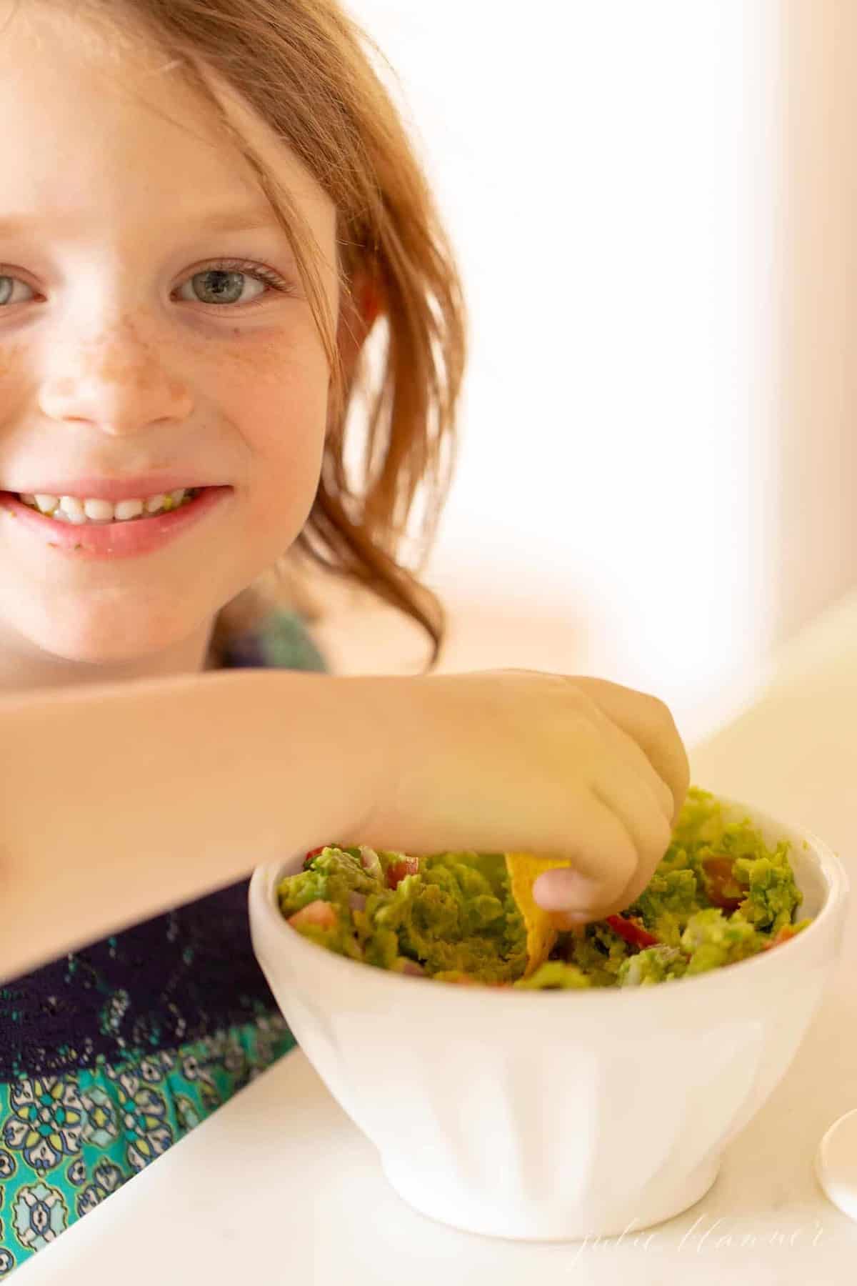 一个小女孩蘸着一碗自制的新鲜鳄梨酱。gydF4y2Ba