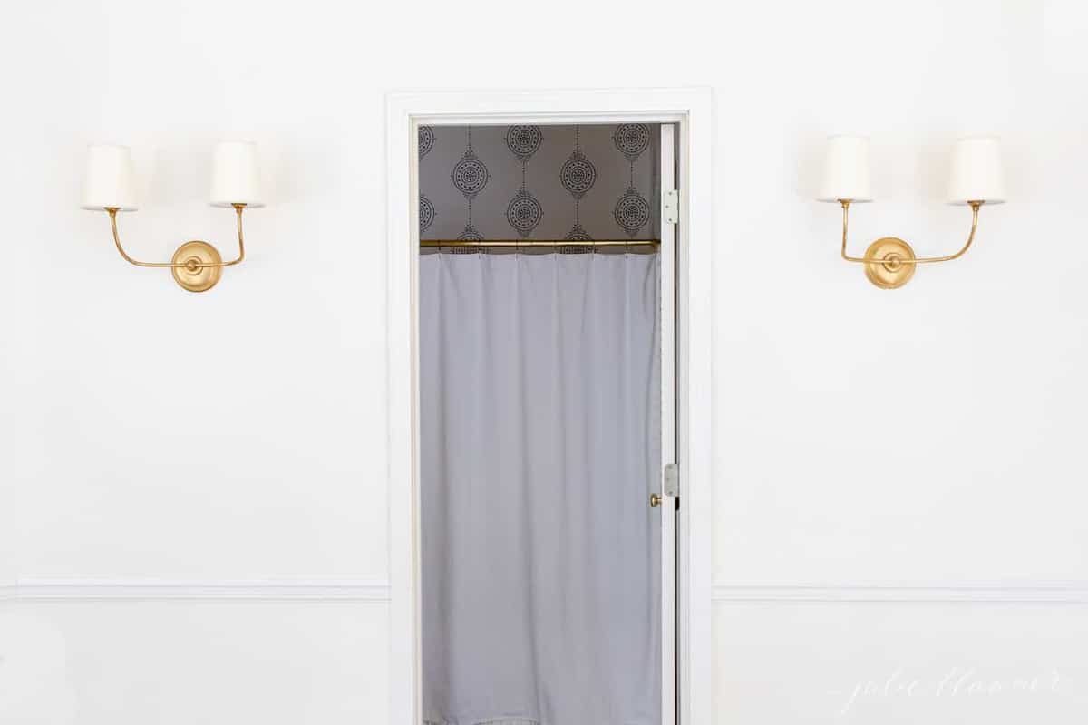 一个白色的彩绘走廊，上面有两个金墙壁灯，门中间打开浴室。