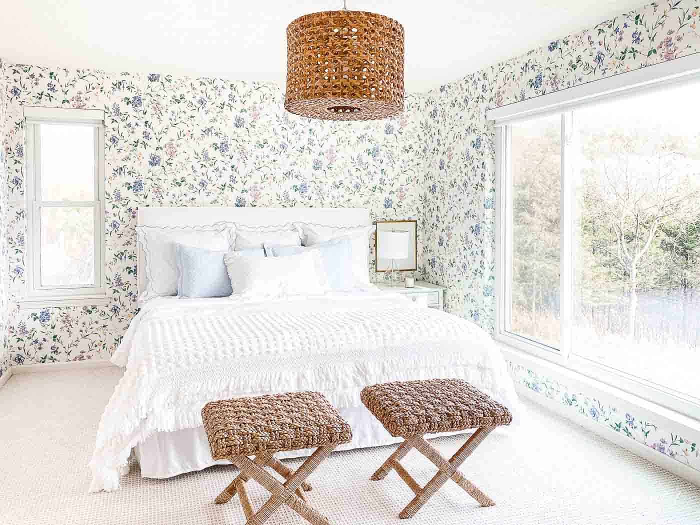 壁纸的卧室，白色的床头板，白色的床上用品和藤条凳子