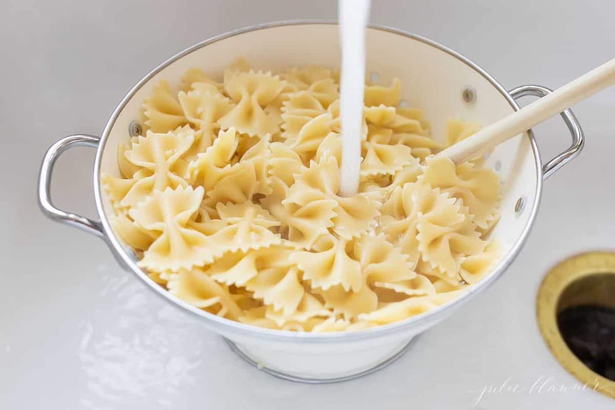 一个带有水的白色漏勺，冲洗煮熟的意大利面，以便如何制作意大利面沙拉。GydF4y2Ba