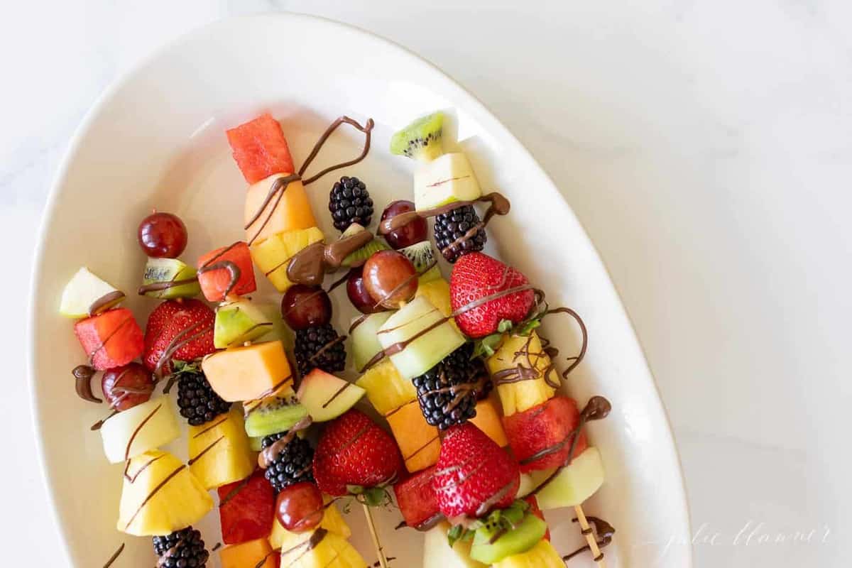 彩色水果串放在白色椭圆形的浅盘上，上面撒着巧克力。