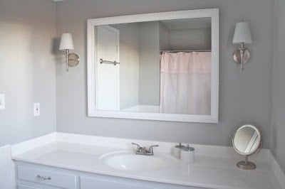 浴室有一个白色的橱柜，白色的大镜框镜子和灰色的墙壁。