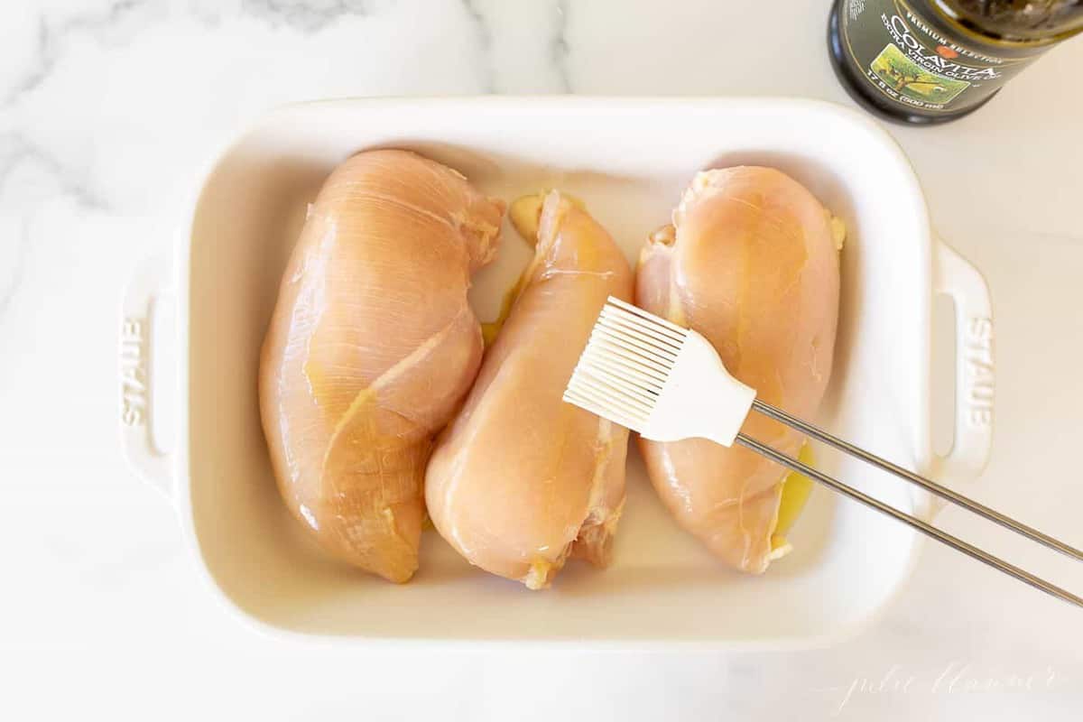 三个生鸡胸放在一个白色的烤盘里，上面刷上白色的油。gydF4y2Ba