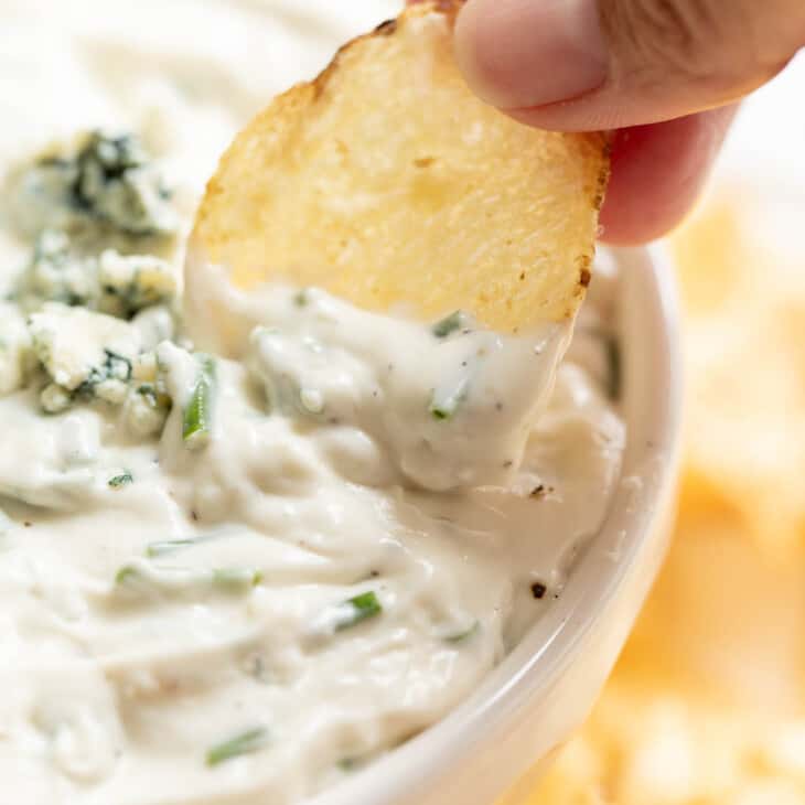 把薯片蘸在白碗里的蓝奶酪酱里
