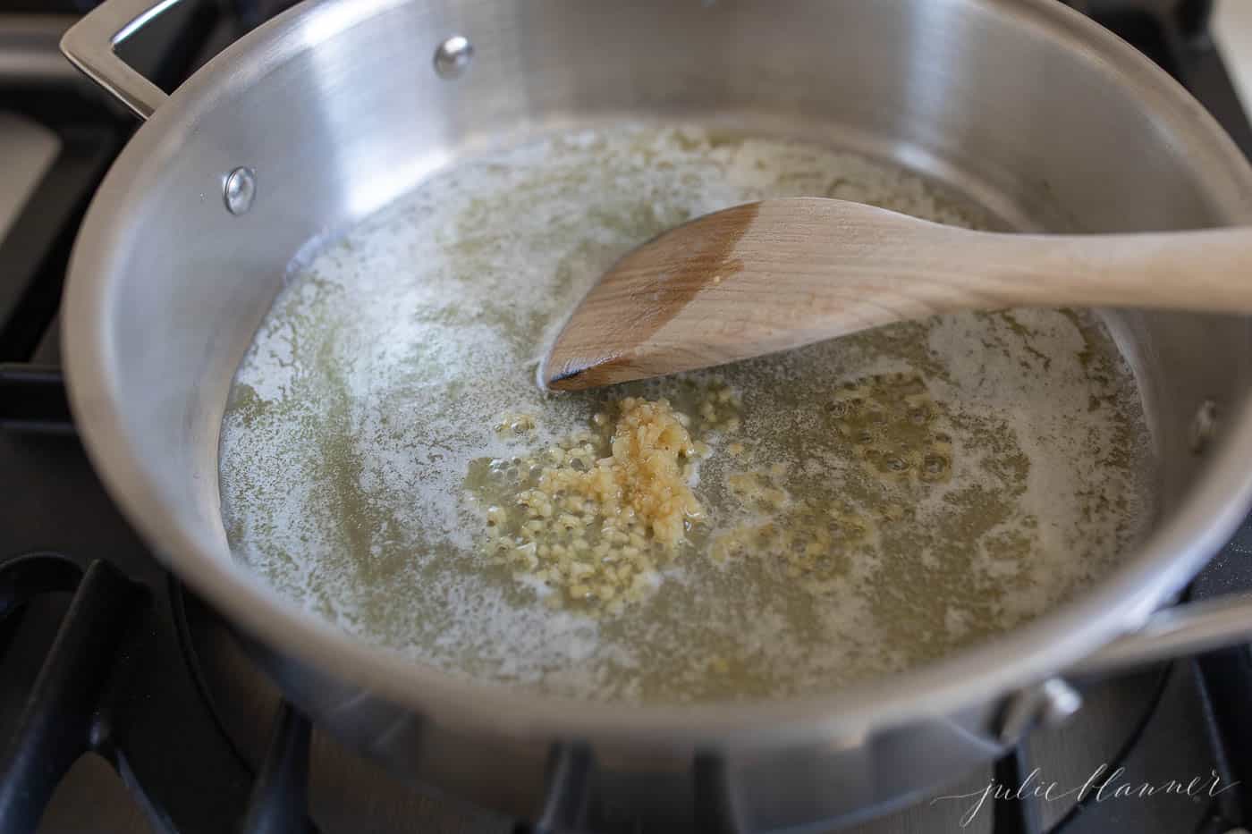 炉子上的一个银锅，融化的黄油和大蒜用木制刮刀搅拌。GydF4y2Ba