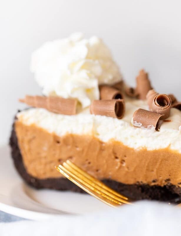 一片法国丝绸饼冠上鞭打奶油和巧克力刨花在白色的板上，金叉到侧面。