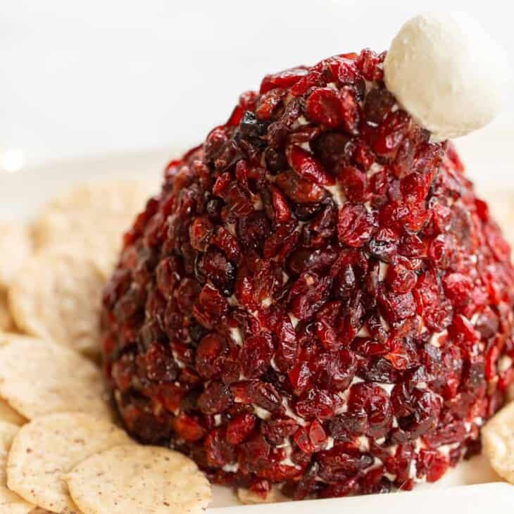 一顶圣诞老人帽子的蔓越莓芝士球，周围是白色盘子上的饼干。GydF4y2Ba