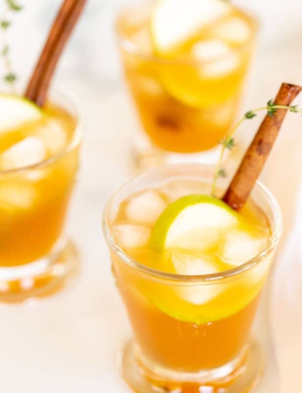 鸡尾酒玻璃杯上装满了苹果酒鸡尾酒，上面装满百里香，肉桂棒和苹果片。