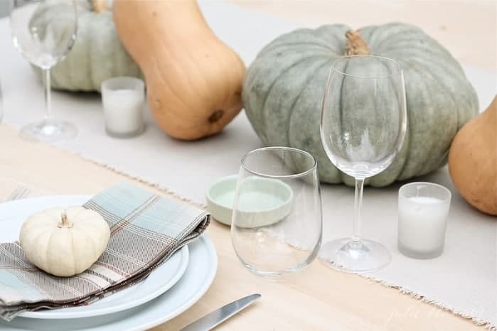 用南瓜和葫芦做成的秋季中心装饰品，配以格纹餐巾的桌子。